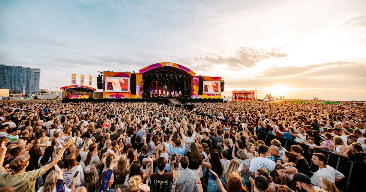Een grote menigte geniet van een concert bij zonsondergang.