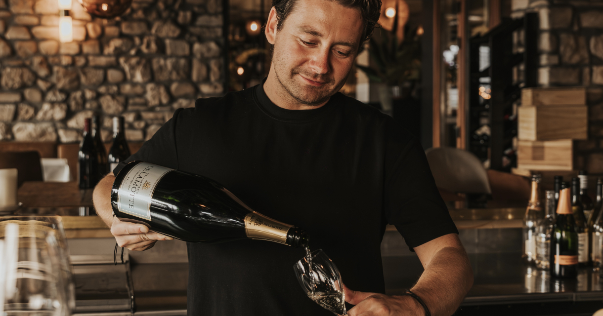 Een bartender schenkt een glass bubbels in.