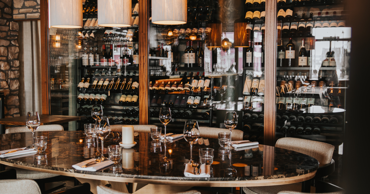 Ronde eettafel met gedekte plaatsen, omringd door moderne stoelen en een glazen wijnkast op de achtergrond