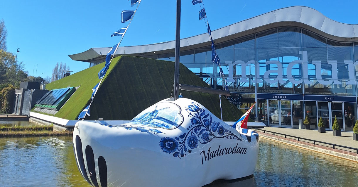 Een grote houten schoenboot voor Madurodam met vlaggen en het gebouw op de achtergrond.
