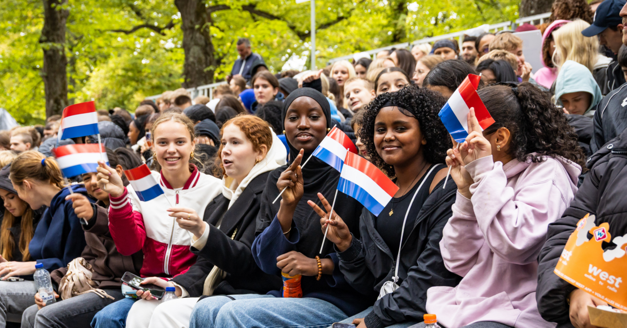 Groep jongeren steunt een evenement met Nederlandse vlaggen.