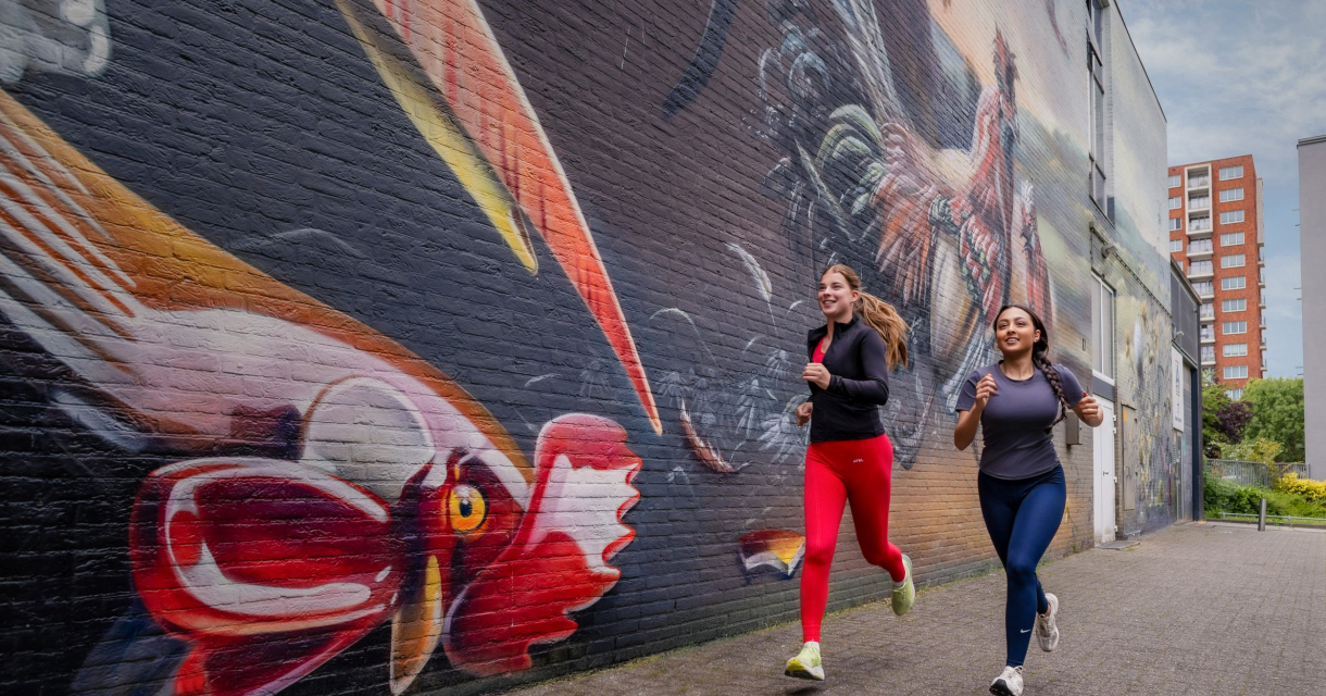 Twee vrouwen joggen langs een gekleurde muurschildering.