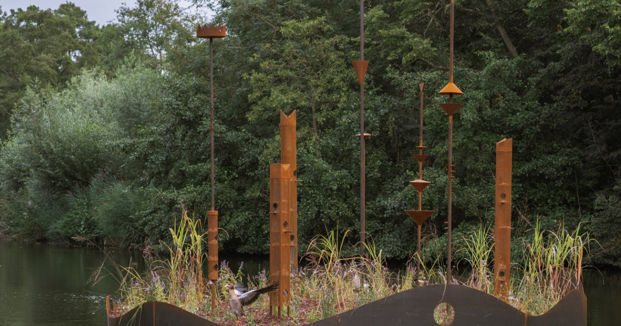 Met gras en bladeren bedekte, metalen sculpturen in het water