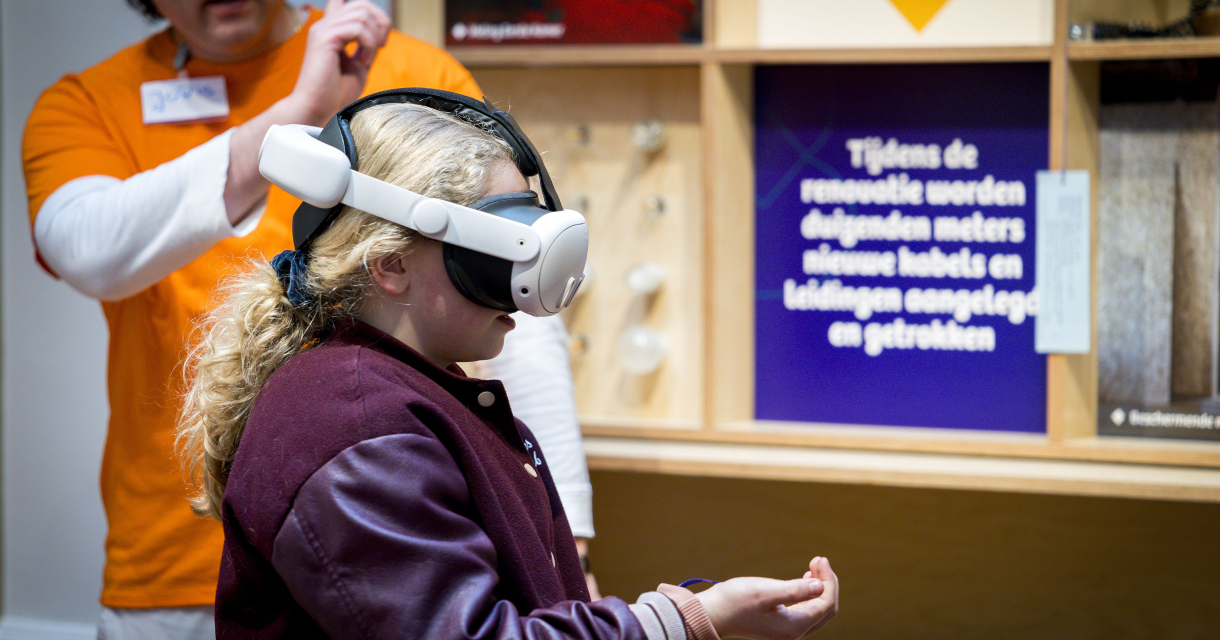 Een meisje met een VR-bril ervaart virtual reality terwijl een begeleider uitlegt.