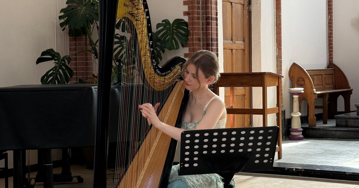 Music on the harp. Een harpiste in een groene jurk speelt een harp in een lichte concertzaal.