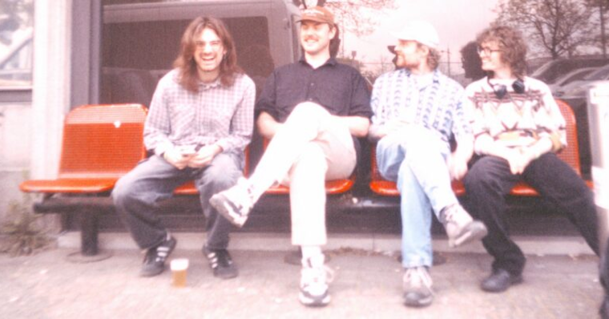 Vier bandleden Lintworm zittend op een bankje, lachend in Den Haag.