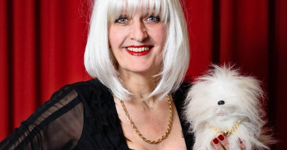 Vrouw met lange witte haren en een faux hondje in haar hand.