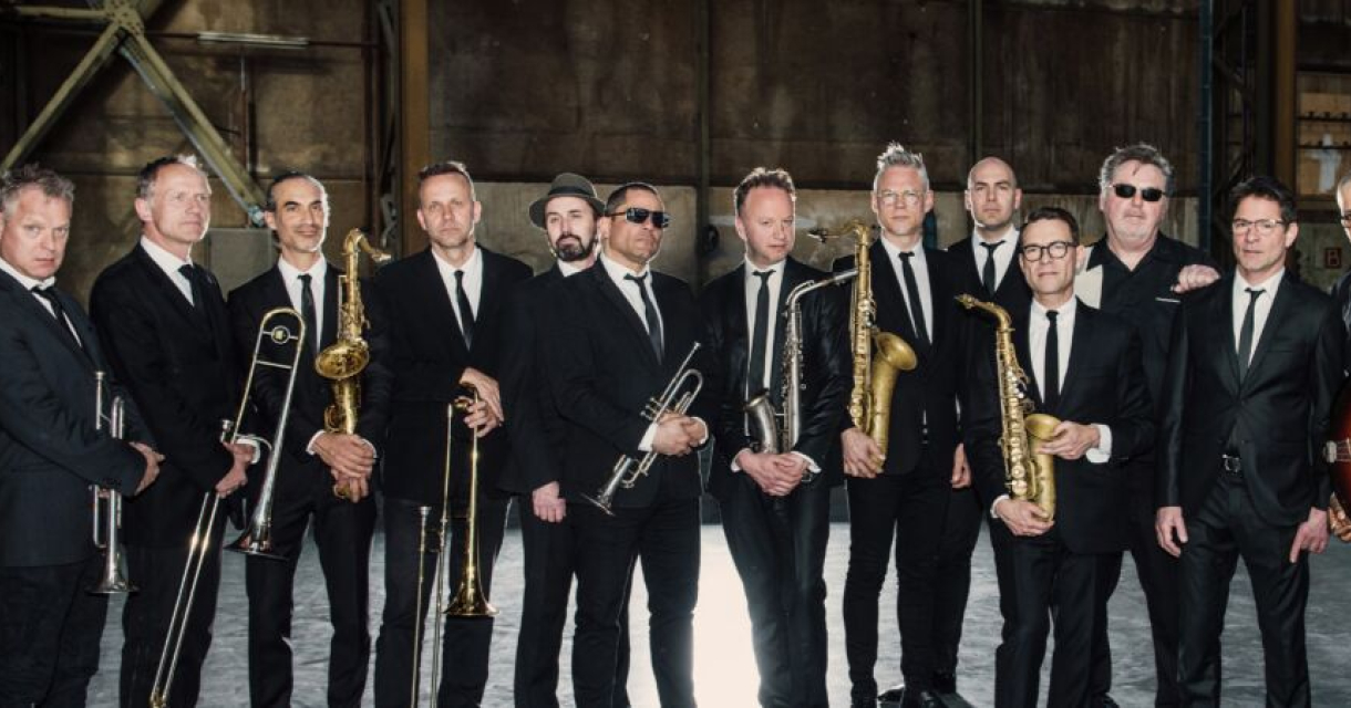 New Cool Collective Big Band in nette zwarte pakken met stropdas poseert voor de lens met hun instrumenten.