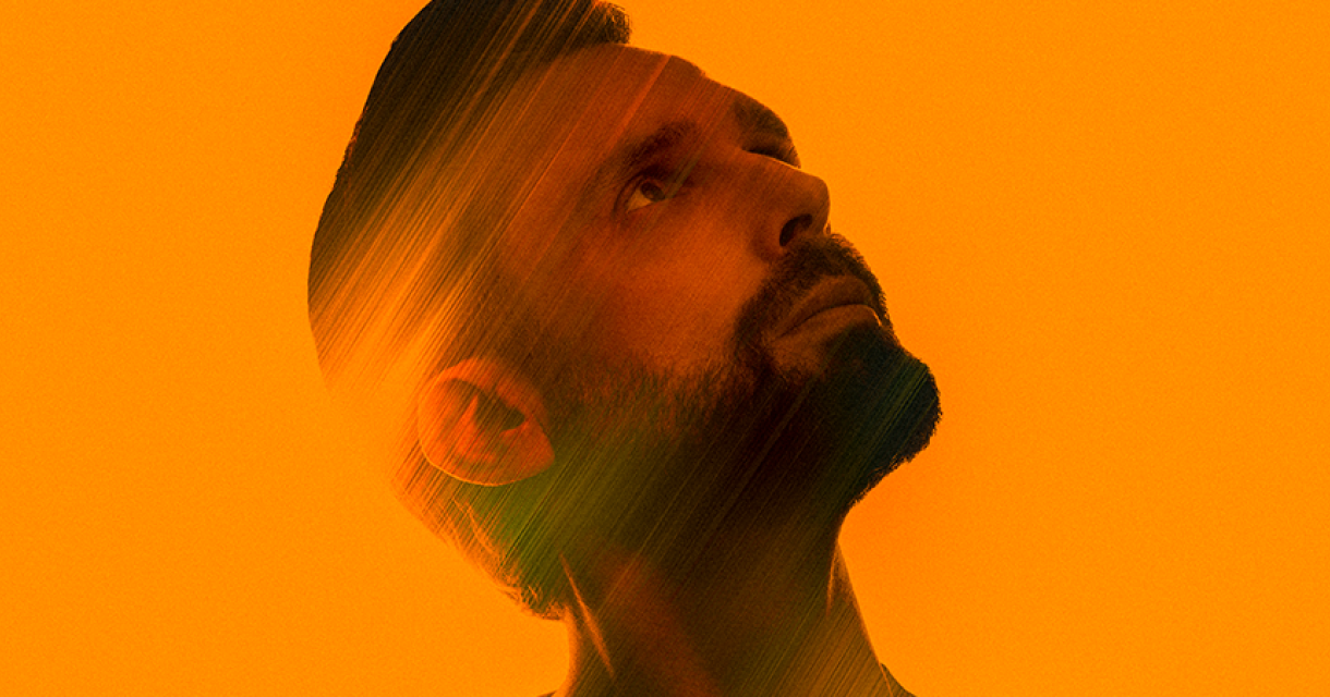 Portret van zanger Nick Schilder schuin omhoog kijkend blendend in de oranje achtergrrond.