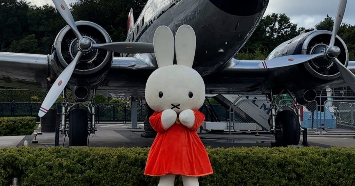Miffy in een rode jurk staat voor een vliegtuig.