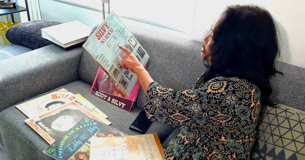 Een vrouw zit op een bank en wijst naar een platenhoes.