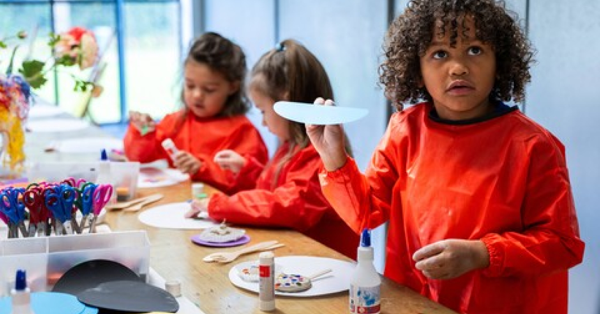 Kinderen in oranje schorten knutselen met papier en lijm.