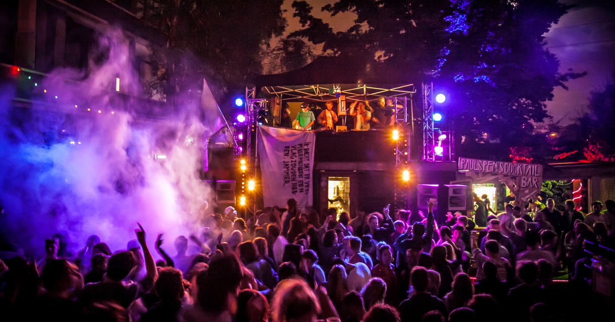 Dansende mensen op een dancefeest in met rook en gekleurd licht. De DJ's staan op een verhoging