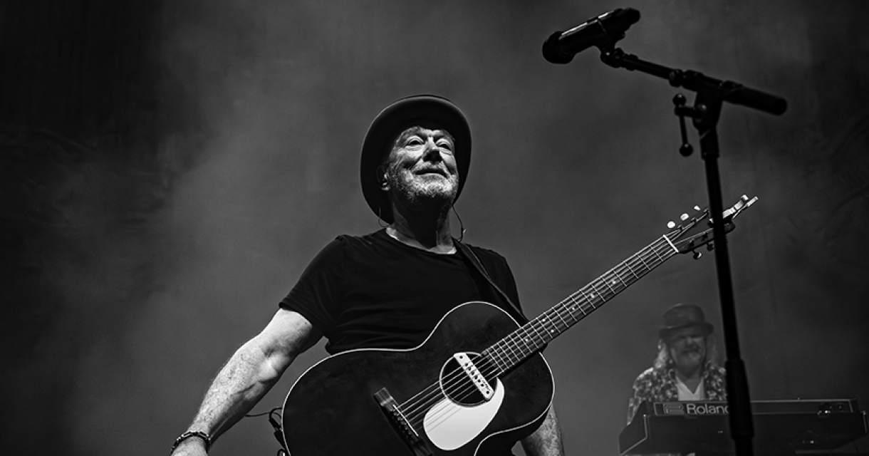 Een zanger met een gitaar staat op het podium met een microfoon.