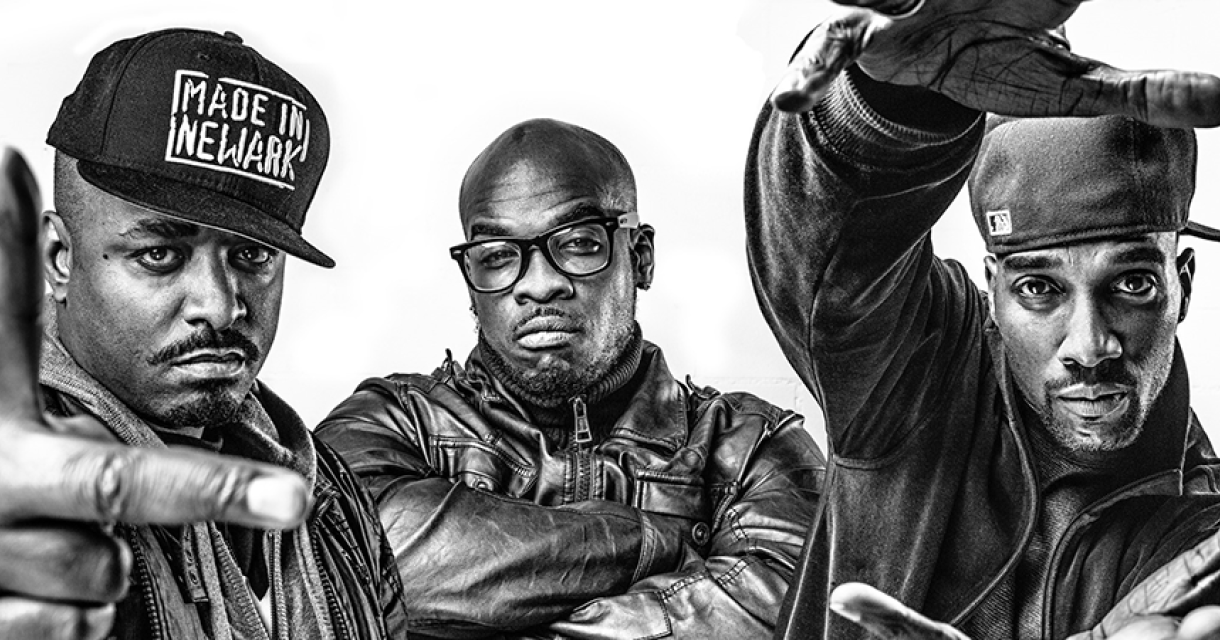 Drie mannen poseren in zwart-wit met stoere houdingen.