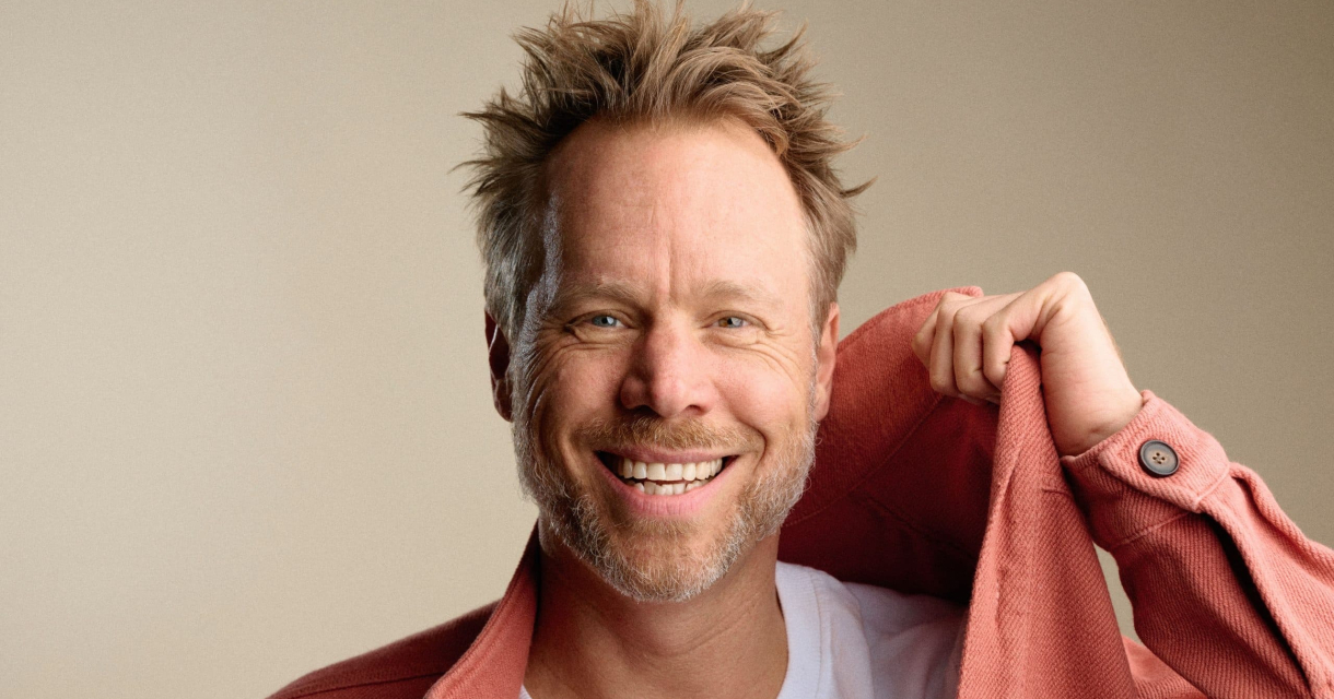 Man met een blij gezicht draagt een roze jas