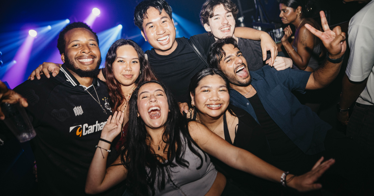 Zeven mensen lachen en poseren samen op een feest