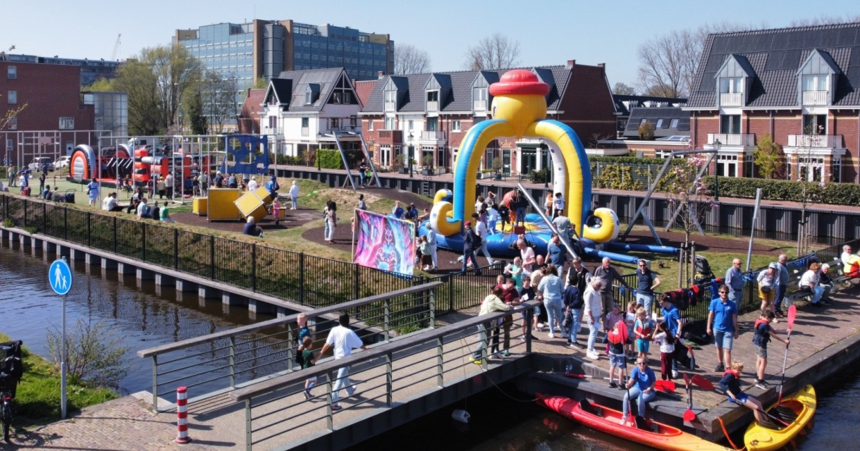 Mensen genieten van een zonnige dag bij een speelplaats met wateractiviteiten en tenten in Den Haag.