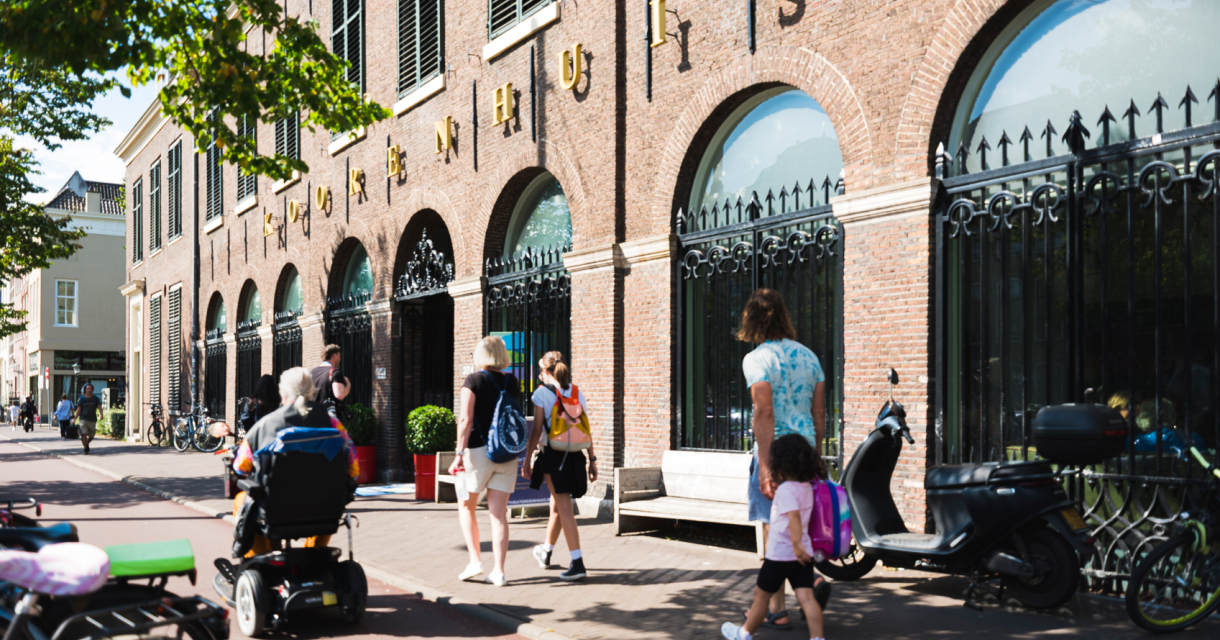 Voorkant van het Koorenhuis op een zonnige dag waar mensen langs lopen en rijden in een scootmobiel