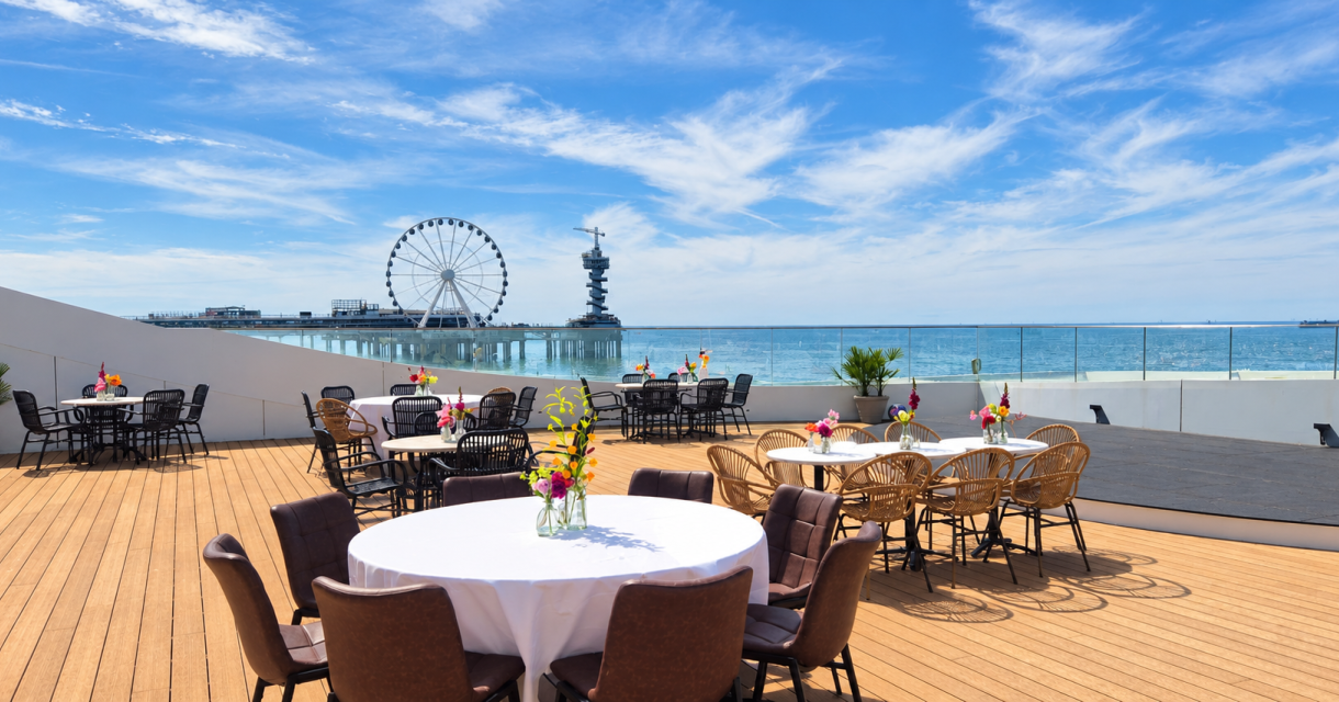 Sonnige Terrasse mit Tischen und Blick auf den Strand und das Riesenrad