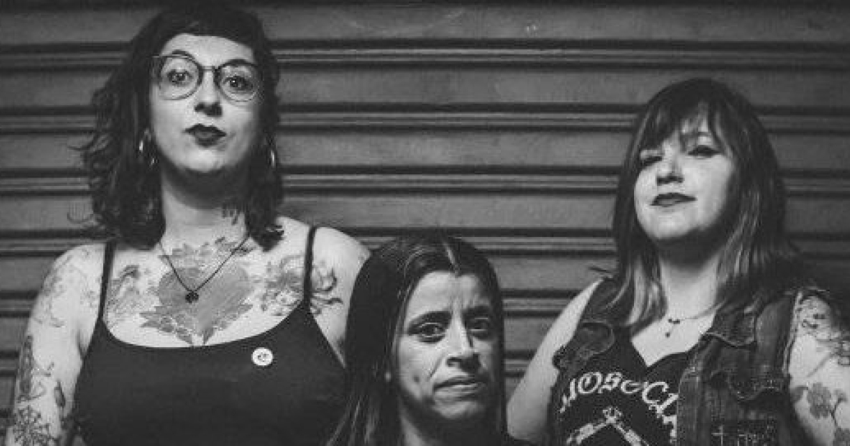 Drie vrouwen met tatoeages, poseren trots voor een muur.