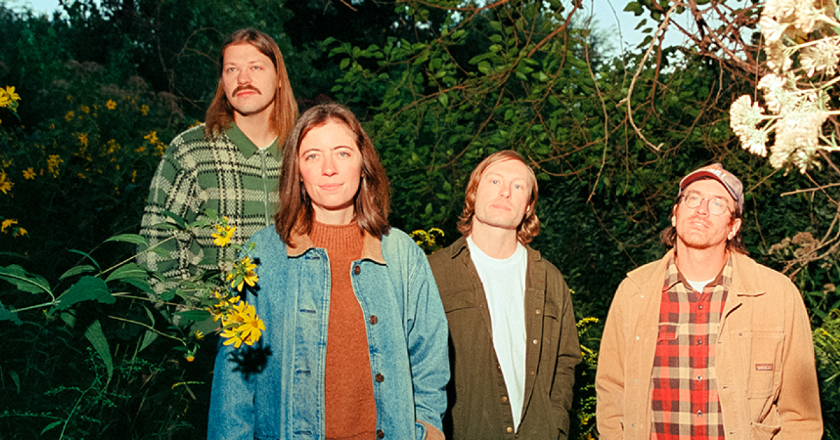 Vier personen staan in een bloemenrijke omgeving.