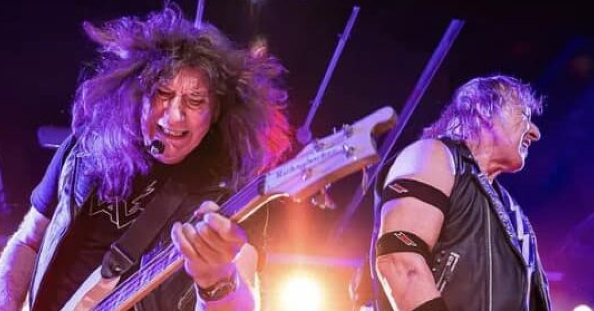 Twee muzikanten van band Raven spelen live op het podium met felle lichten.