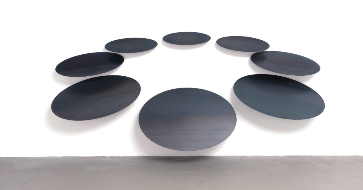 Zwarte, ovale kunstpanelen hangen aan een witte muur.