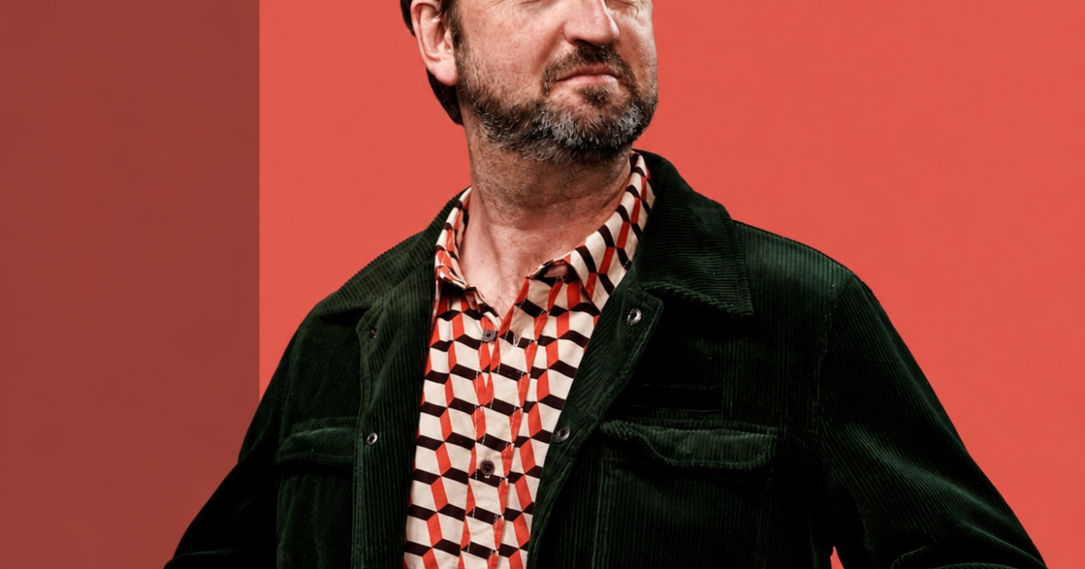Man met een baard in een groene jas en een geometrisch shirt