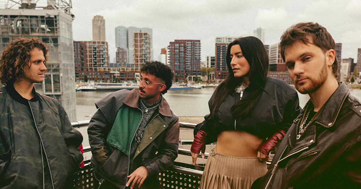 Vijf mensen van de band Rondé staan op een balkon met een stedelijke achtergrond.