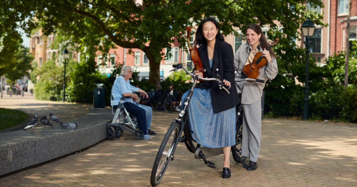 Twee vrouwen met violen fietsen door de stad.
