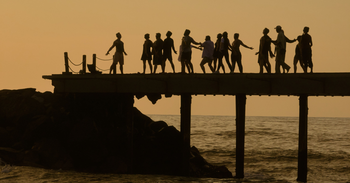 Silhouetten van mensen die op een pier dansen bij zonsondergang