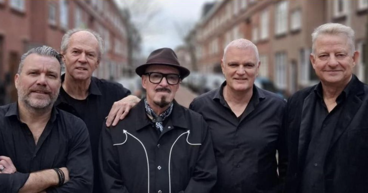 Vijf mannen in zwarte kleding poseren op een straat.