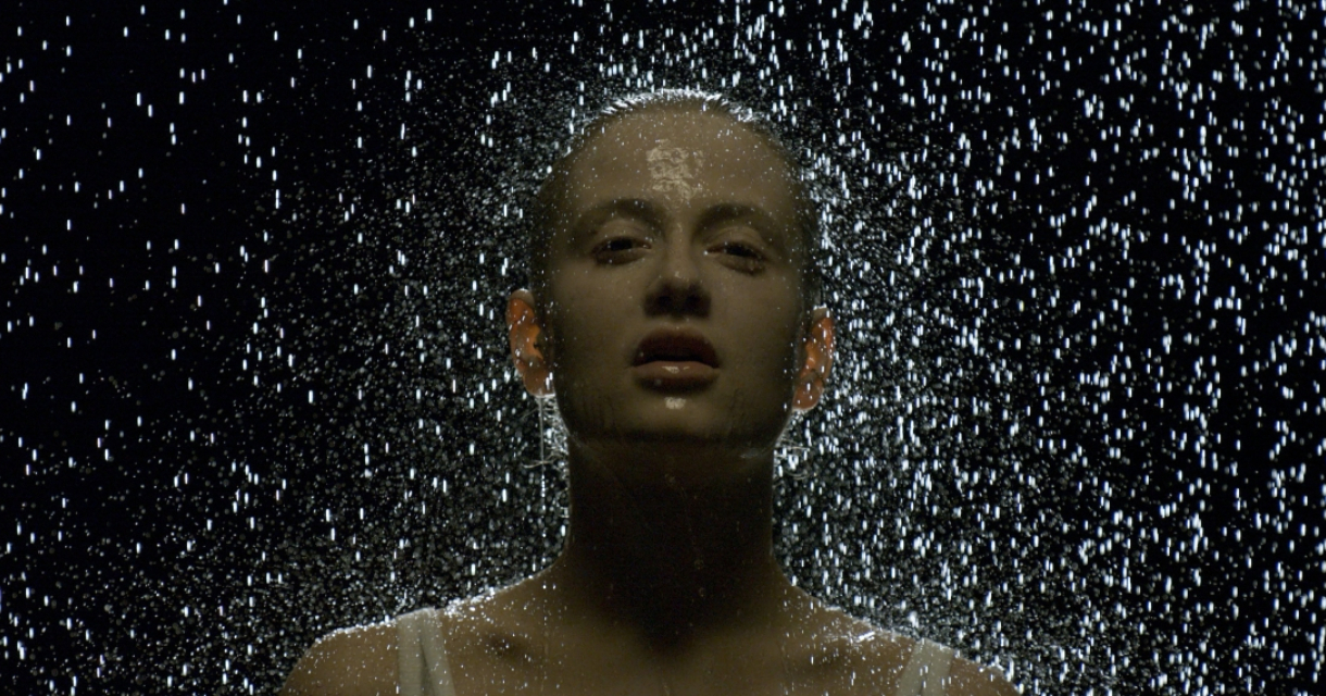 Een persoon staat onder vallend water met een donkere achtergrond.