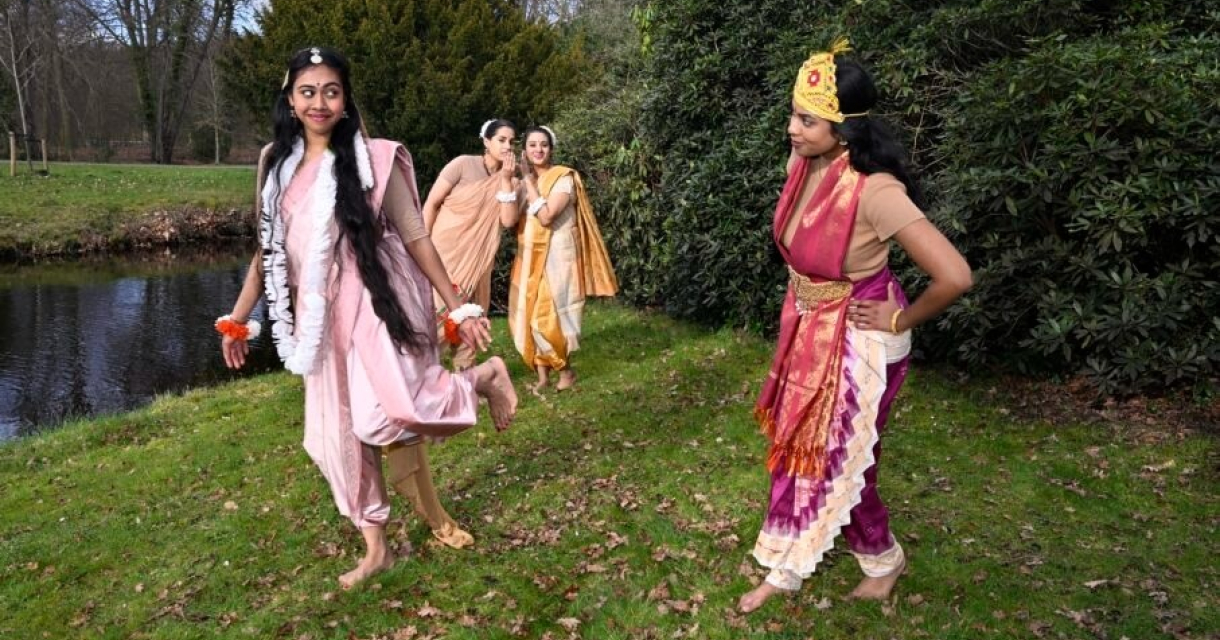 Vier vrouwen in traditionele kleding poseren bij een natuurwater.