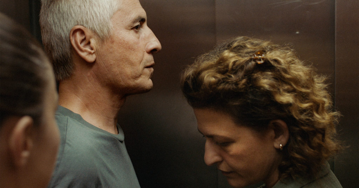 Three people stand in an elevator, looking serious.
