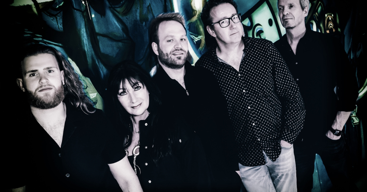 Vijf muzikanten poseren voor een kunstzinnige muur.