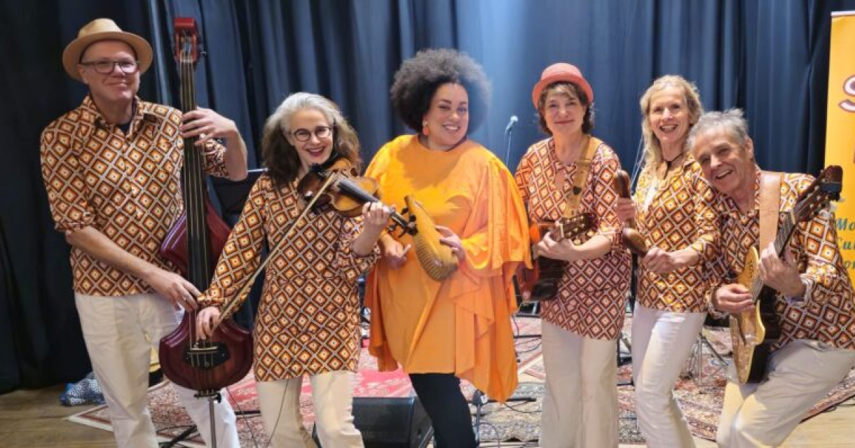 Zes bandleden van SonPaTí poseren samen. Ze kijken recht in de camera en stralen energie en verbondenheid uit. De sfeer is informeel en muzikaal. Instrumenten zoals viool, gitaar en percussie zijn zichtbaar.