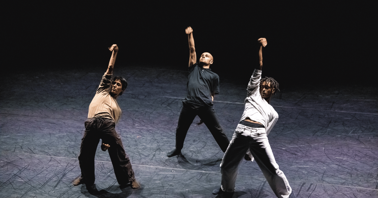 Three dancers performing a choreography on stage.
