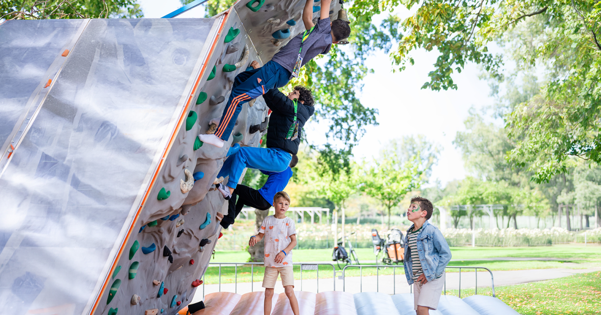 Stadsspelen Den Haag. Kinderen proberen te klimmen op een verticale klimwand in een park.