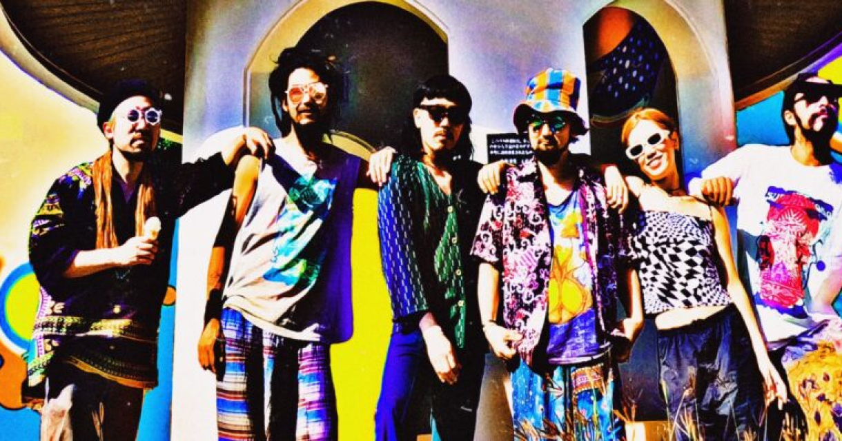 De bandleden van Super Jet Kinoko poseren in een holografische setting, omringd door lichtprojecties en transparante kleurreflecties. De compositie geeft een futuristisch en vervreemdend effect, passend bij hun trance-achtige stijl.