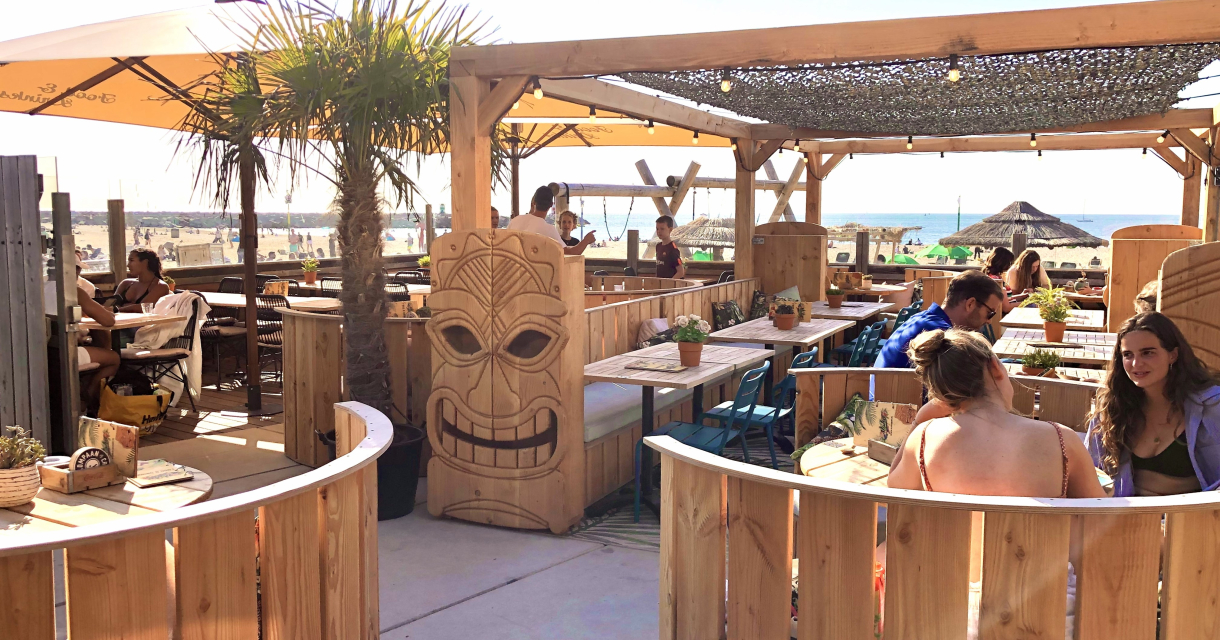 Eine sonnige Strandbar mit Holzmöbeln und Palmen.