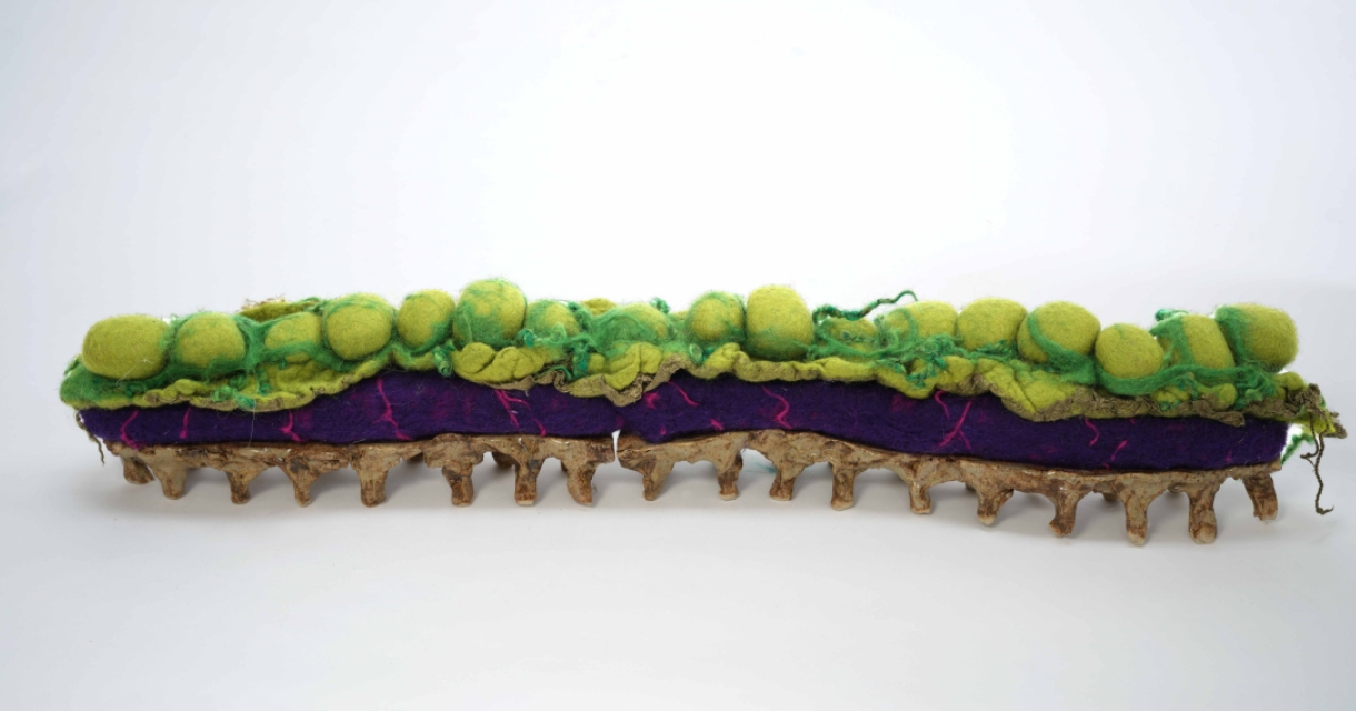 Textiel als taal. Een langwerpig viltkunstwerk met groene bollen en paarse ondergrond.