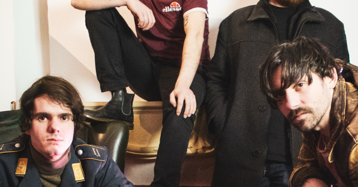 Vier mannen poseren in een woonkamer met een open haard.