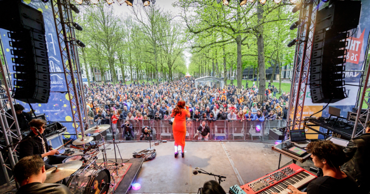 Zangeres op het podium op het Lange Voorhout tijdens The Life I Live. Ze is van achter gefotografeerd waardoor je het drukke publiek ziet.