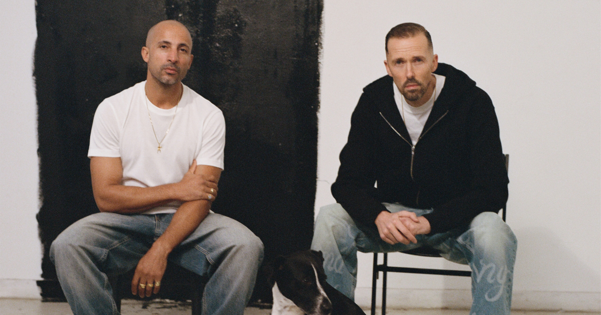 Twee mannen The Opposites zitten op stoelen met een hond voor hen.