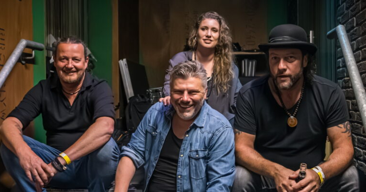 De band zit lachend op een trap, klaar voor hun optreden.