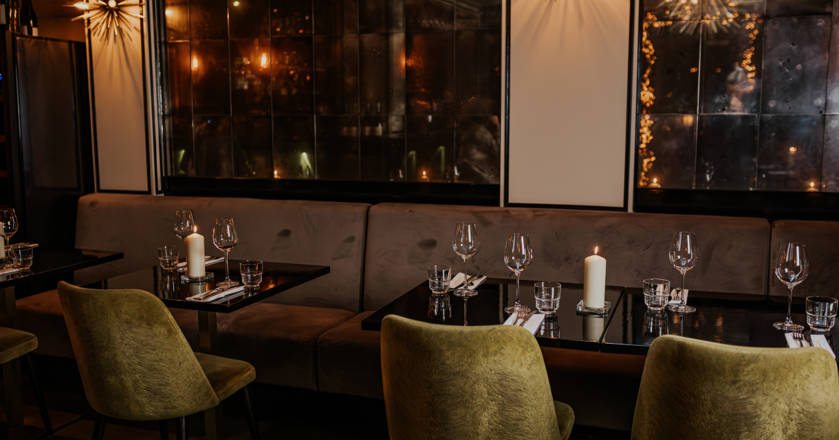 Gedekte tafels met kaarslicht, fluwelen stoelen en spiegelwanden in een sfeervol restaurantinterieur