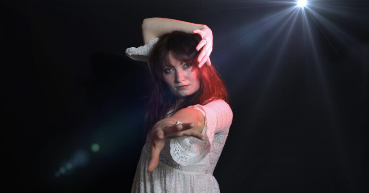 Vrouw in een witte jurk met uitgestrekte arm en lichteffecten geïnspireerd op icon Kate Bush.