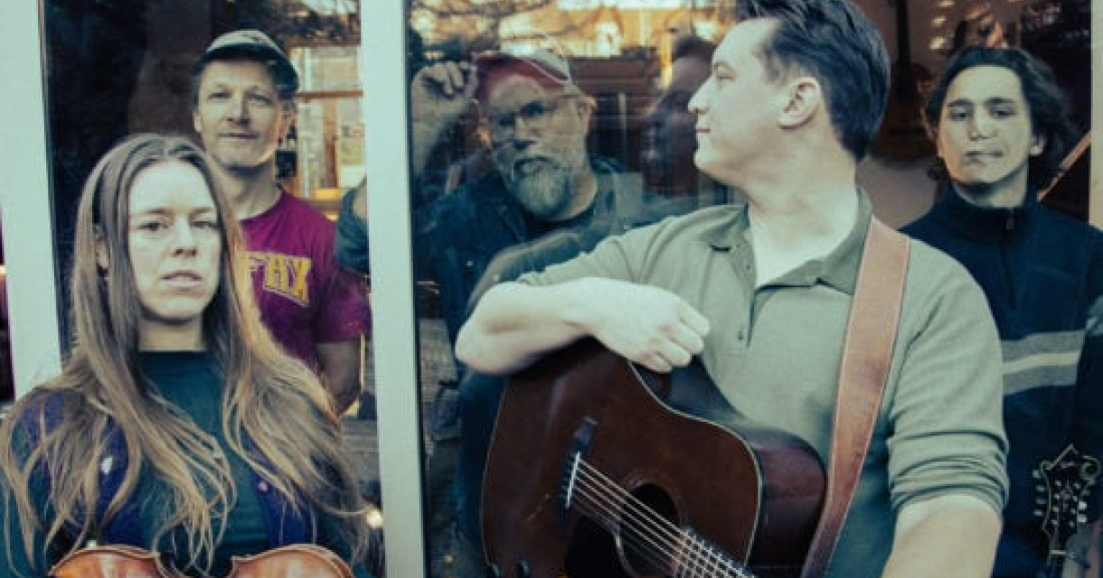 Groep muzikanten met een viool en gitaar, staand achter glas. Foto: Kees-Wevers